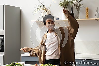 Excited joyful millennial African girl cooking and dancing in kitchen Stock Photo