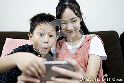 Excited kid boy and child girl are enjoying playing online game on mobile phone,siblings having fun relaxing together,children Stock Photo