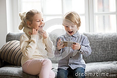 Excited kids having fun using smartphone sitting together on sof Stock Photo