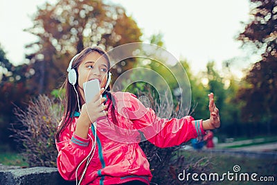 Excited little girl dancing, singing and listening music with headphones and smart phone outdoor Stock Photo