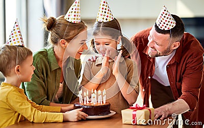 Excited little girl looking at cake and making wish while celebrating Birthday with family at home Stock Photo