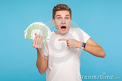 Excited man in t-shirt being surprised to hold big money, pointing to euro bills in hand and looking with shocked amazed Stock Photo