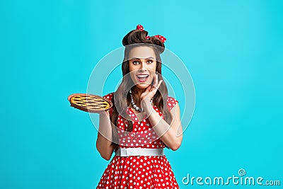 Excited pinup retro style housewife holding homemade pie, feeling excited on blue studio background Stock Photo