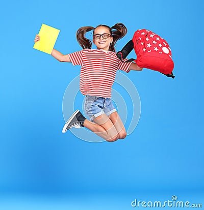 Excited schoolgirl in glasses jumping up from happiness and joy with backpack and exercise book in hands Stock Photo