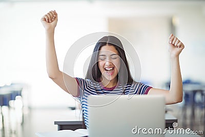 Excited schoolgirl sitting with laptop in classroom Stock Photo