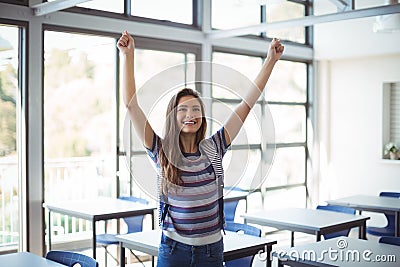 Excited schoolgirl standing with arms up in classroom Stock Photo