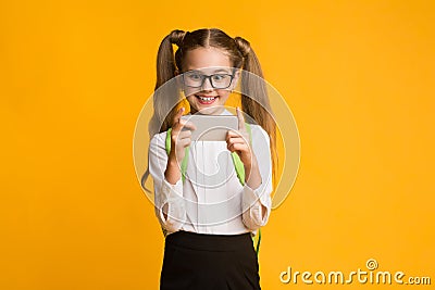 Excited Schoolgirl Using Smartphone Playing Game During Break, Studio Shot Stock Photo