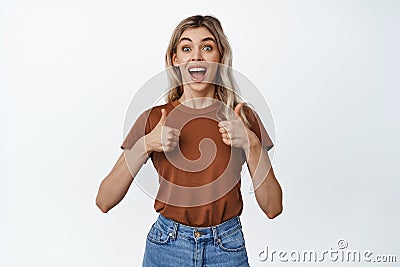 Excited smiling woman showing thumbs up, positive reaction to something great, standing amazed against white background Stock Photo