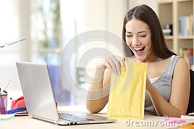 Excited student opening padded envelope at home Stock Photo