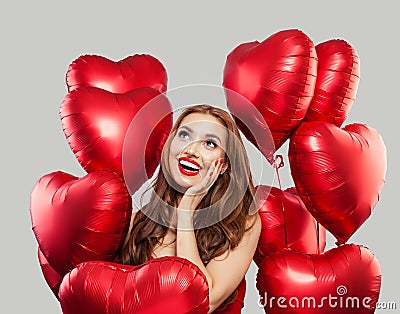 Excited woman with red heart balloons on white background. Happy surprised model girl with red lips makeup, long curly hair. Gift Stock Photo