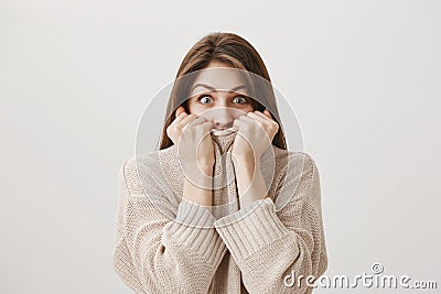 Excited woman trying to control emotions hearing shocking rumor. Emotive good-looking girl pulling sweater on face and Stock Photo