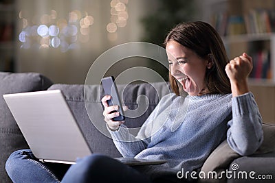 Excited woman using phone and laptop in the night Stock Photo