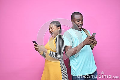 excited young black people standing back to back viewing contents on their phones, looking surprised, young african man and woman Stock Photo
