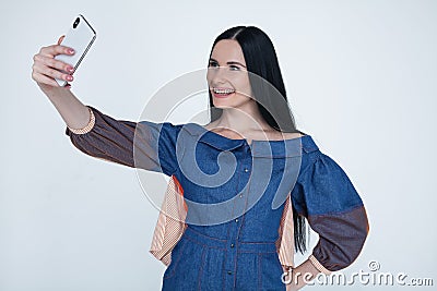 Excited young brunette woman making selfie using smart phone. Student girl with long hair in jeans shirt taking photograph with Stock Photo