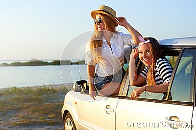 Two women enjoying road trip on a summer day at seaside. Excited young female friends leaning out of car windows and Stock Photo