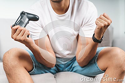 Excited young handsome man playing video game and raising fists sitting on the couch at home Stock Photo