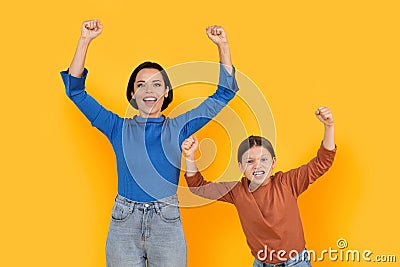 Excited Young Mother And Little Daughter Celebrating Success Over Yellow Studio Background Stock Photo