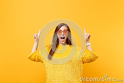 Excited young woman in fur sweater and heart orange glasses pointing index fingers up on copy space isolated on bright Stock Photo