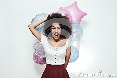 Excitement and happiness. Surprised young afro american woman holding colourful balloons, looking at camera and smiling Stock Photo