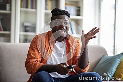 Exciting african american guy sitting at home, watching tv Stock Photo