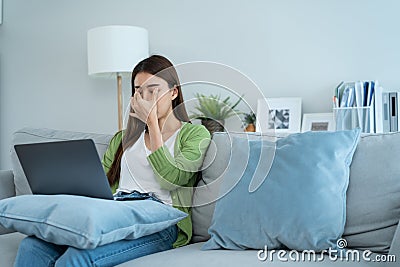 Exhausted Asian business woman hurt eye while using laptop computer. Young girl office worker sit on sofa feel visual fatigue and Stock Photo