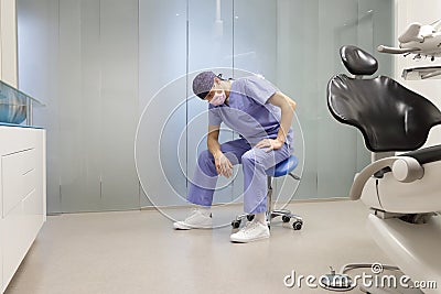 Exhausted dentist sitting on dental saddle - price of success Stock Photo