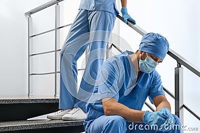 Exhausted doctors on stairs indoors. Stress of health care workers during COVID-19 pandemic Stock Photo