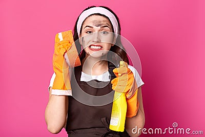 Exhausted emotional cleaner standing isolated over pink background in studio, holding washcloth near ear and detergent, having Stock Photo