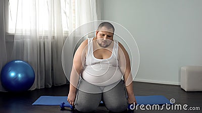 Exhausted fat man sitting on floor with dumbbells, tiring workout program, sport Stock Photo