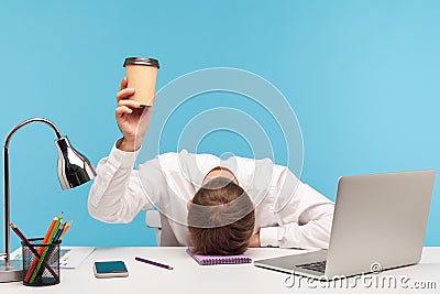 Exhausted male employee feeling fatigue lying on table and raising coffee cup, lack of energy in morning office Stock Photo