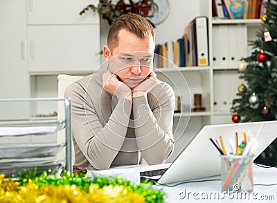 Exhausted male office worker sitting at his desk in Christmas decorated office Stock Photo