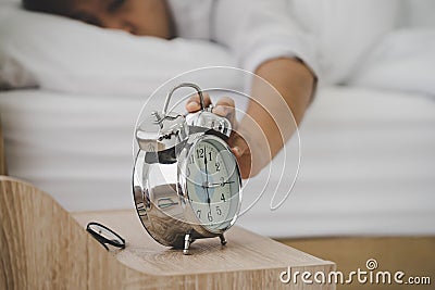 Exhausted man sleeping in bed tired by waking up to the alarm clock ring in the morning suffering from insomnia Stock Photo