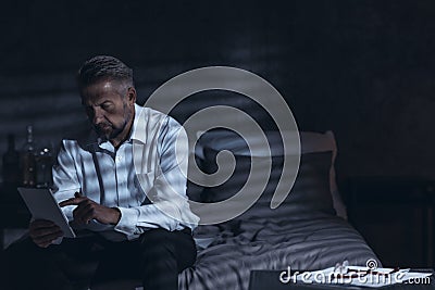 Exhausted middle-aged male sitting on a bed in a hotel room at n Stock Photo