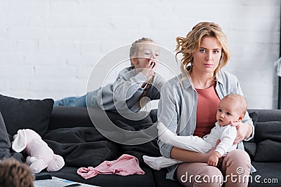 exhausted mother holding infant child and looking at camera while naughty daughter Stock Photo