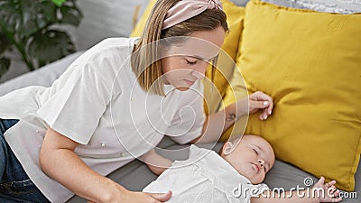 Exhausted mother lying on bed, lovingly watchful while her baby daughter sleeps in bedroom amidst the wholesome family background Stock Photo