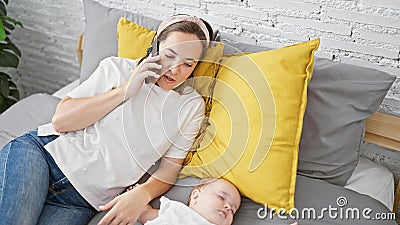 Exhausted mother talking on smartphone in a relaxed tone while her lovely daughter sleeps peacefully on the bed in their cozy Stock Photo