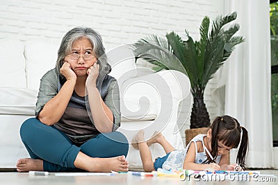 Exhausted old elderly grandmother sit on floor in living room and feel unwell tired from little children running and playing loud Stock Photo