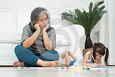 Exhausted old elderly grandmother sit on floor in living room and feel unwell tired from little children running and playing loud Stock Photo