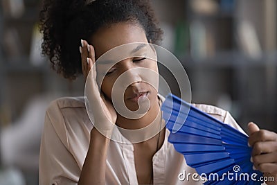 Exhausted overheated young african woman waving paper fan. Stock Photo