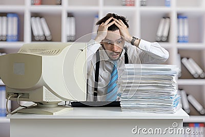 Exhausted overworked man is looking on pile of documents on desk. Paperwork concept. Stock Photo