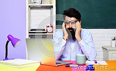 Exhausted stressed teacher suffering from headache sitting at desk in classroom. Tired male student feeling migraine Stock Photo