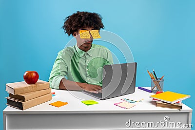 Exhausted teen guy with painted eyes on stickers sitting at desk using laptop, sleeping over blue background Stock Photo