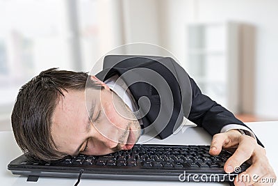 Exhausted or tired businessman is sleeping on keyboard in office Stock Photo