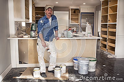 Male painter holding wet paintbrush standing in messy home kitchen fixer upper remodel project, dripping paint cans everywhere Stock Photo