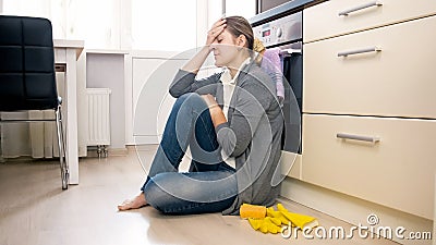 Exhausted woman sitting on floor at kitchen after cleaning house Stock Photo