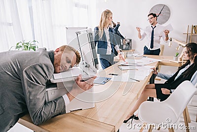 exhausted zombie like businessman sleeping on copier while his colleagues having conversation Stock Photo