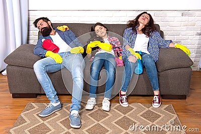 Exhausting cleaning day. Family mom dad and daughter with cleaning supplies sit on couch. Family care about cleanliness Stock Photo