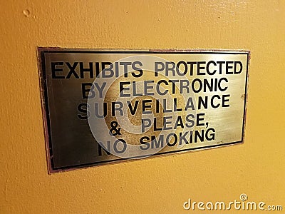 Exhibits protected by electronic surveillance and please no smoking sign on yellow wall Stock Photo