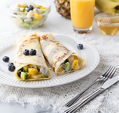 Exotic fruit crepes on a white plate surrounded by juice, honey and fruit. Stock Photo