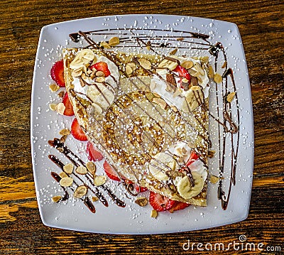 Triangle shaped dessert crepe served with creme fraiche, strawberries, almonds, drizzled chocolate sauce. Stock Photo